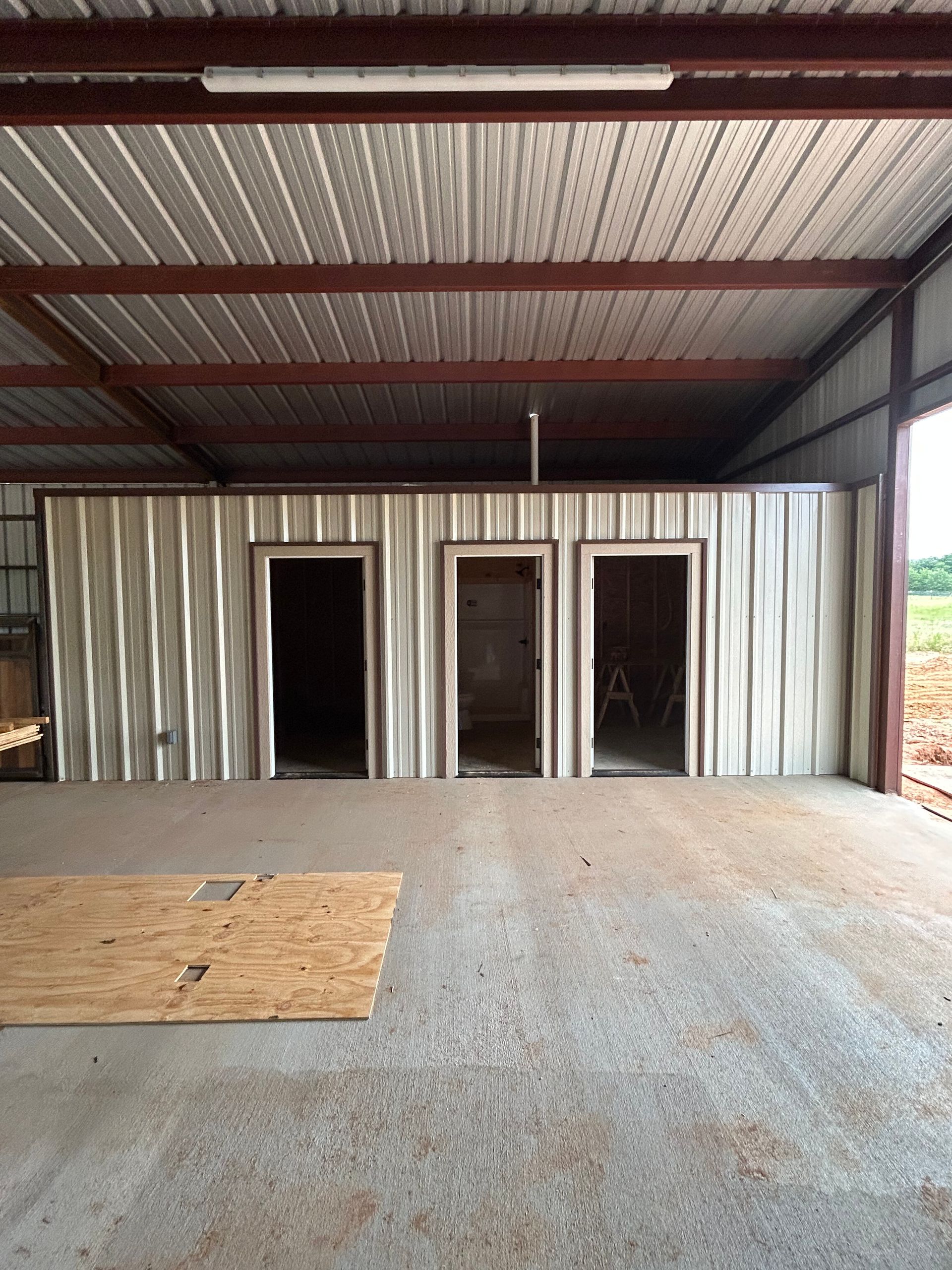 Interior of a metal building with three doorways and a concrete floor under a red steel roof