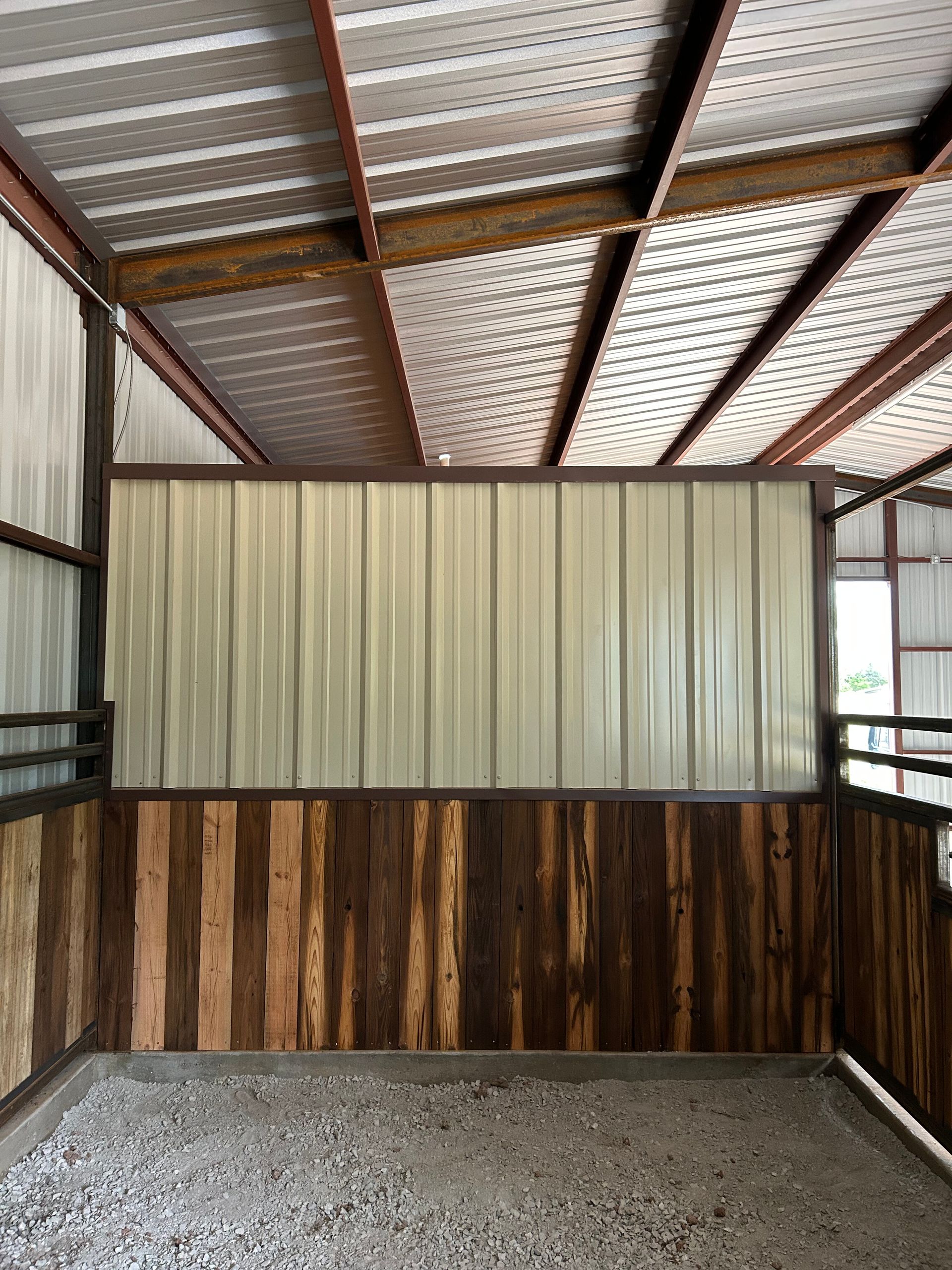 Empty metal shed interior with corrugated roof, beige wall panels, and gravel floor