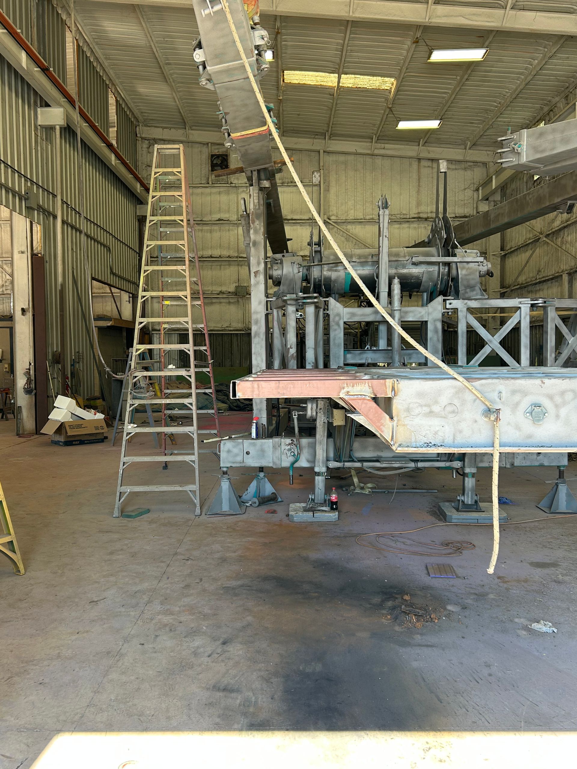 Interior of an industrial warehouse with ladders, scaffolding, and large equipment under repair