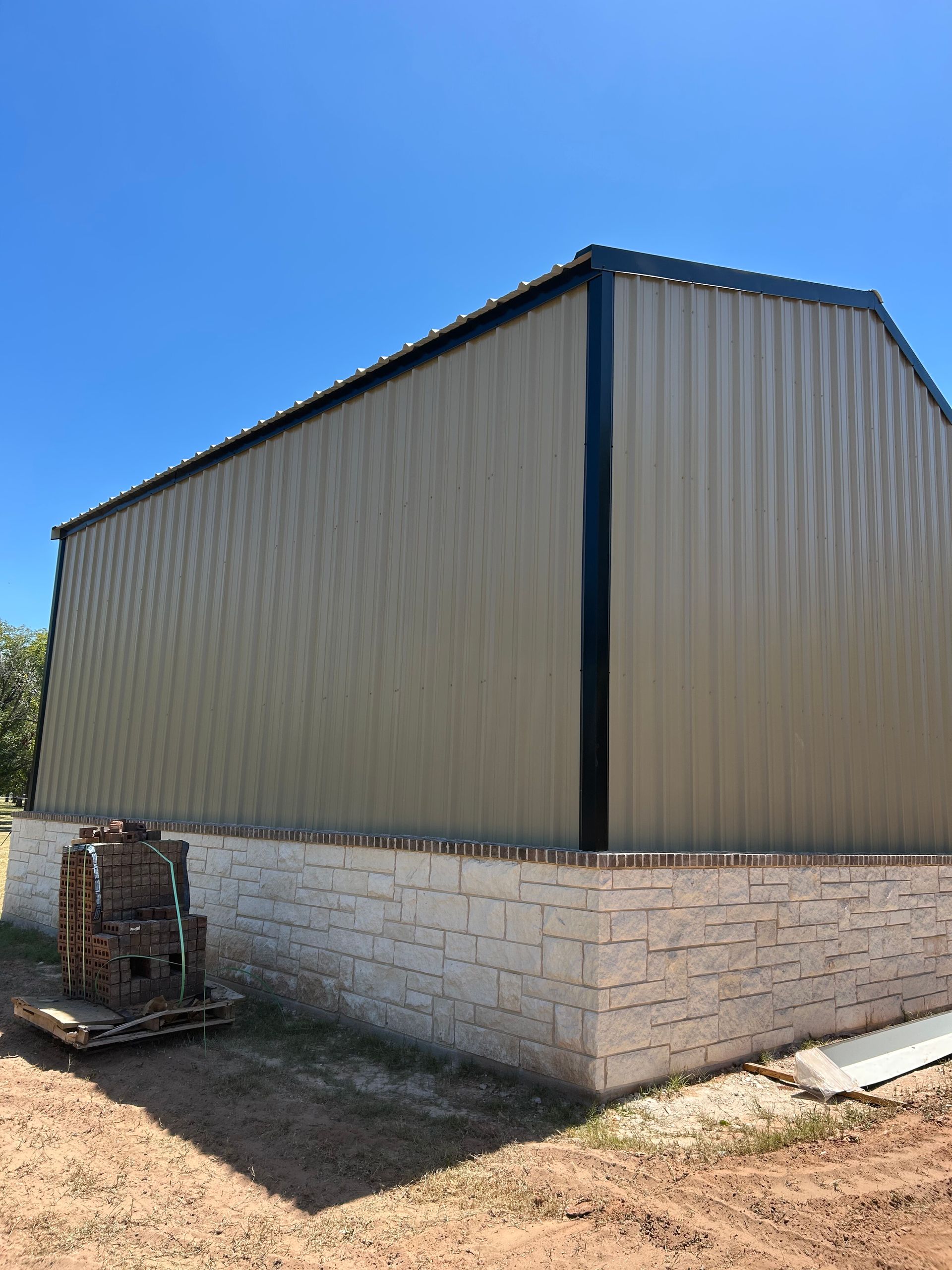 Large tan metal shed with a white block foundation under a blue sky.