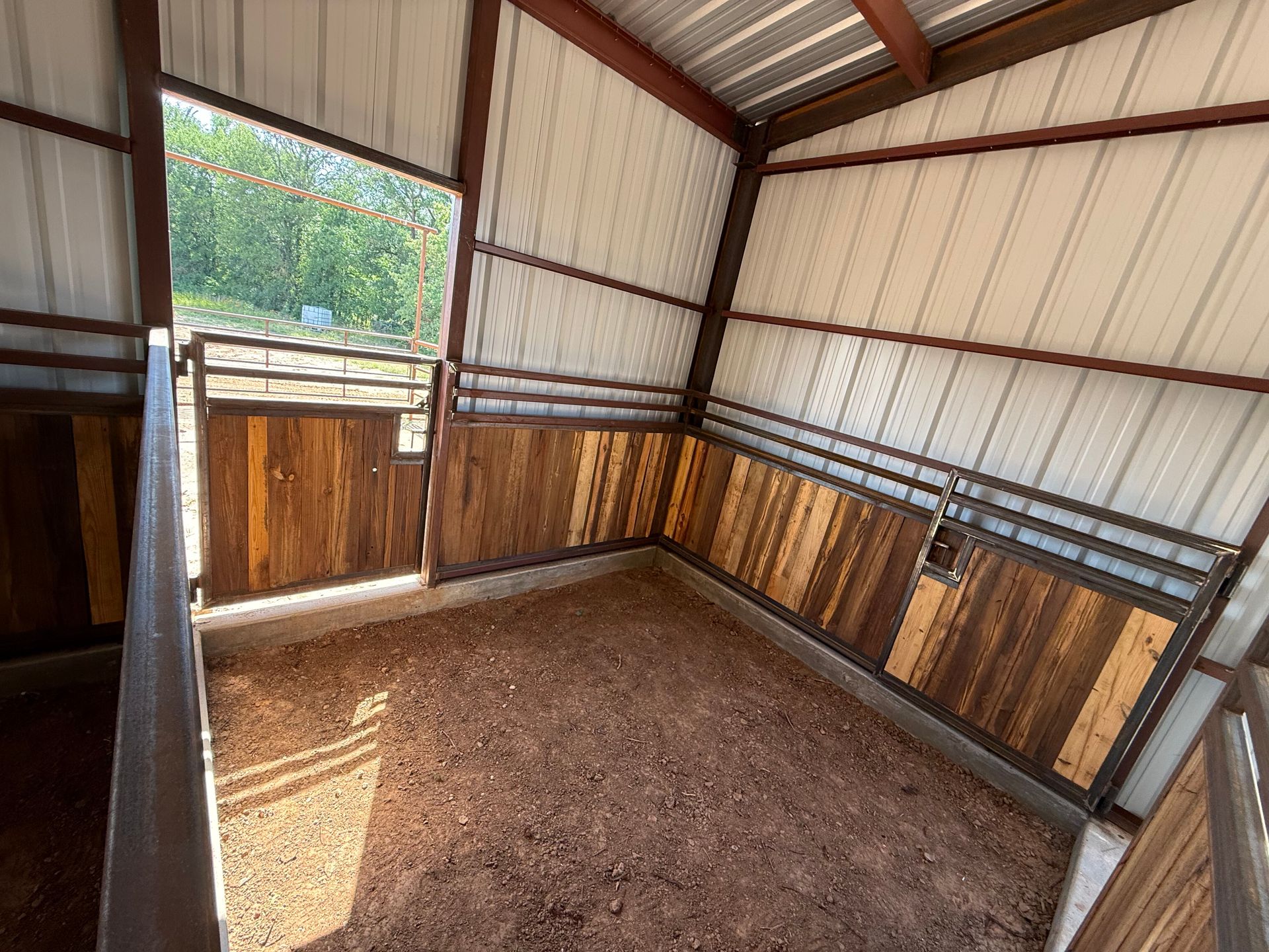 Small empty metal shed with wood walls, dirt floor, and a half-open wooden door letting in light.