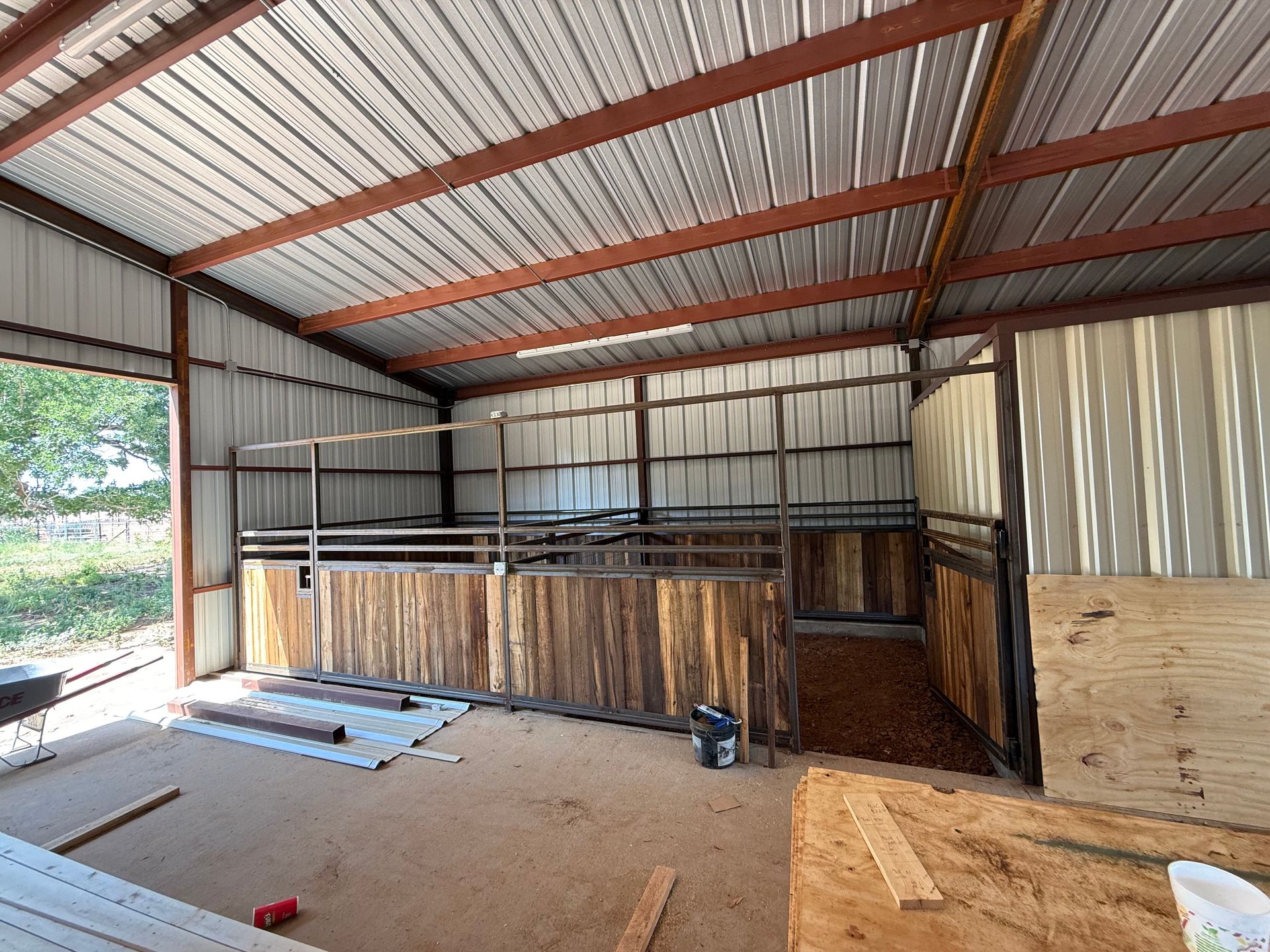 Empty metal barn interior with corrugated walls, wood beams, and stacked lumber by the back wall