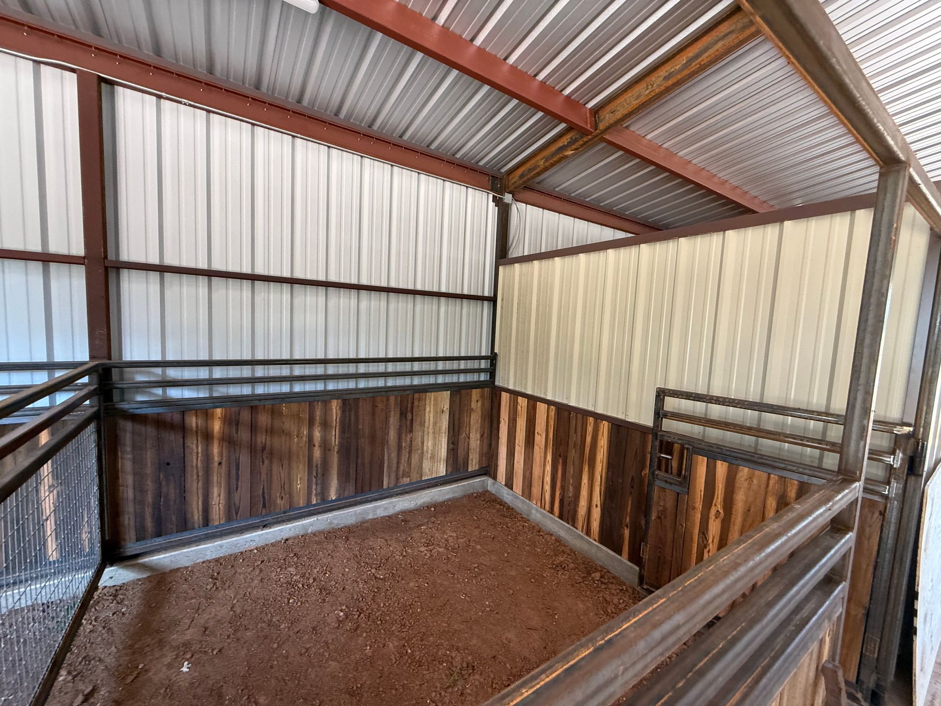 Small livestock pen with corrugated metal roof, wooden walls, and dirt floor