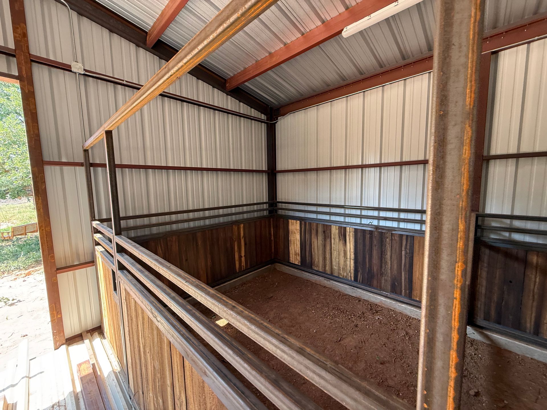 Empty metal livestock stall inside a corrugated shed with wooden posts and rails
