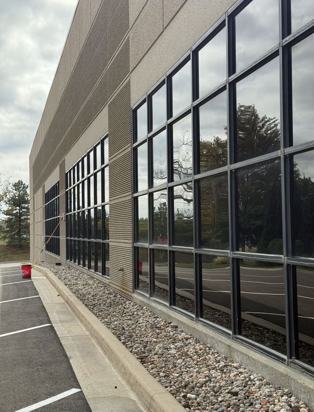Modern building exterior with large reflective windows beside a parking lot and gravel border