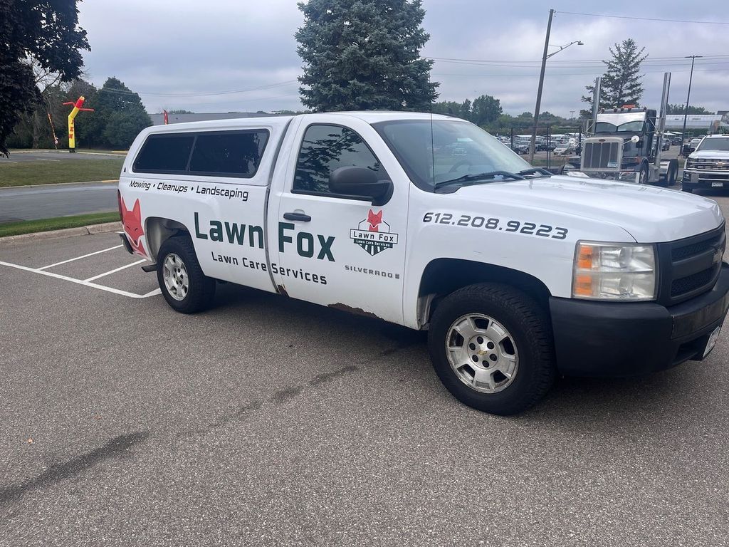 White Lawn Fox pickup truck parked in a lot, with logo and contact info on the side.