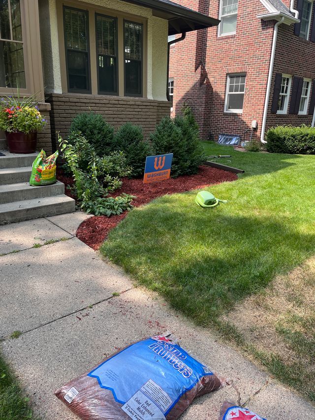 Front lawn with a house, sidewalk, flower beds, and bags of mulch near the steps.