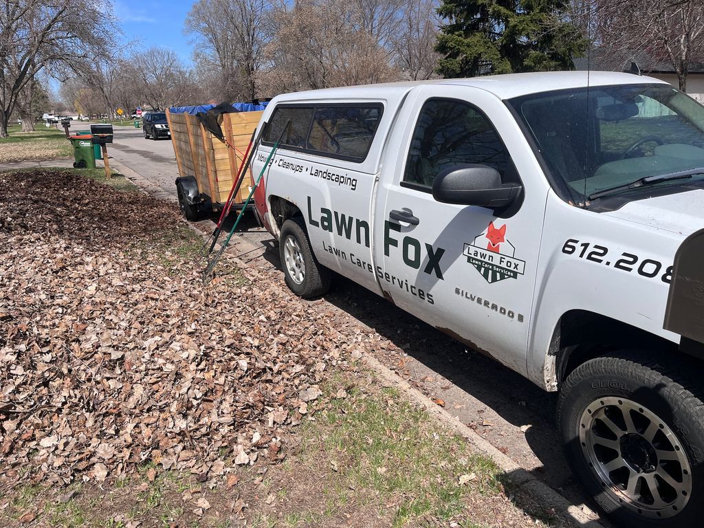 Lawn Fox service truck with trailer parked along a leaf-covered curb on a suburban street.
