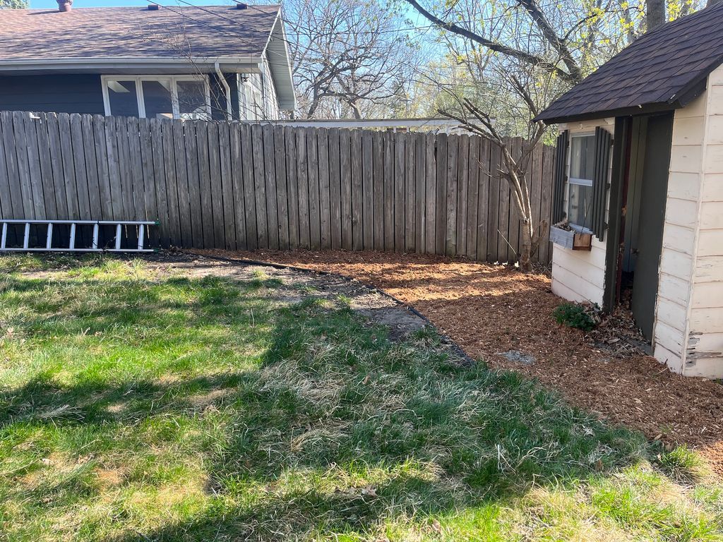 Backyard with patchy grass, wooden fence, and a house wall beside a small shed.
