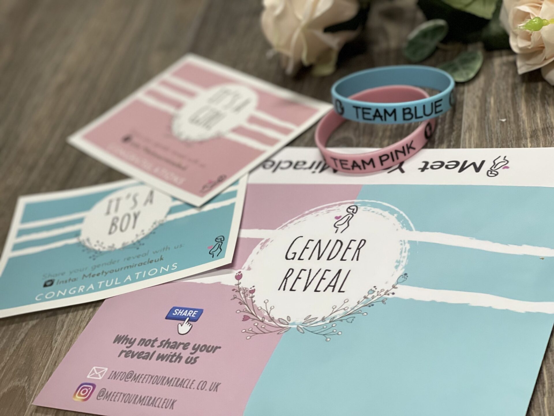 A gender reveal cards and bracelets are sitting on a wooden table.