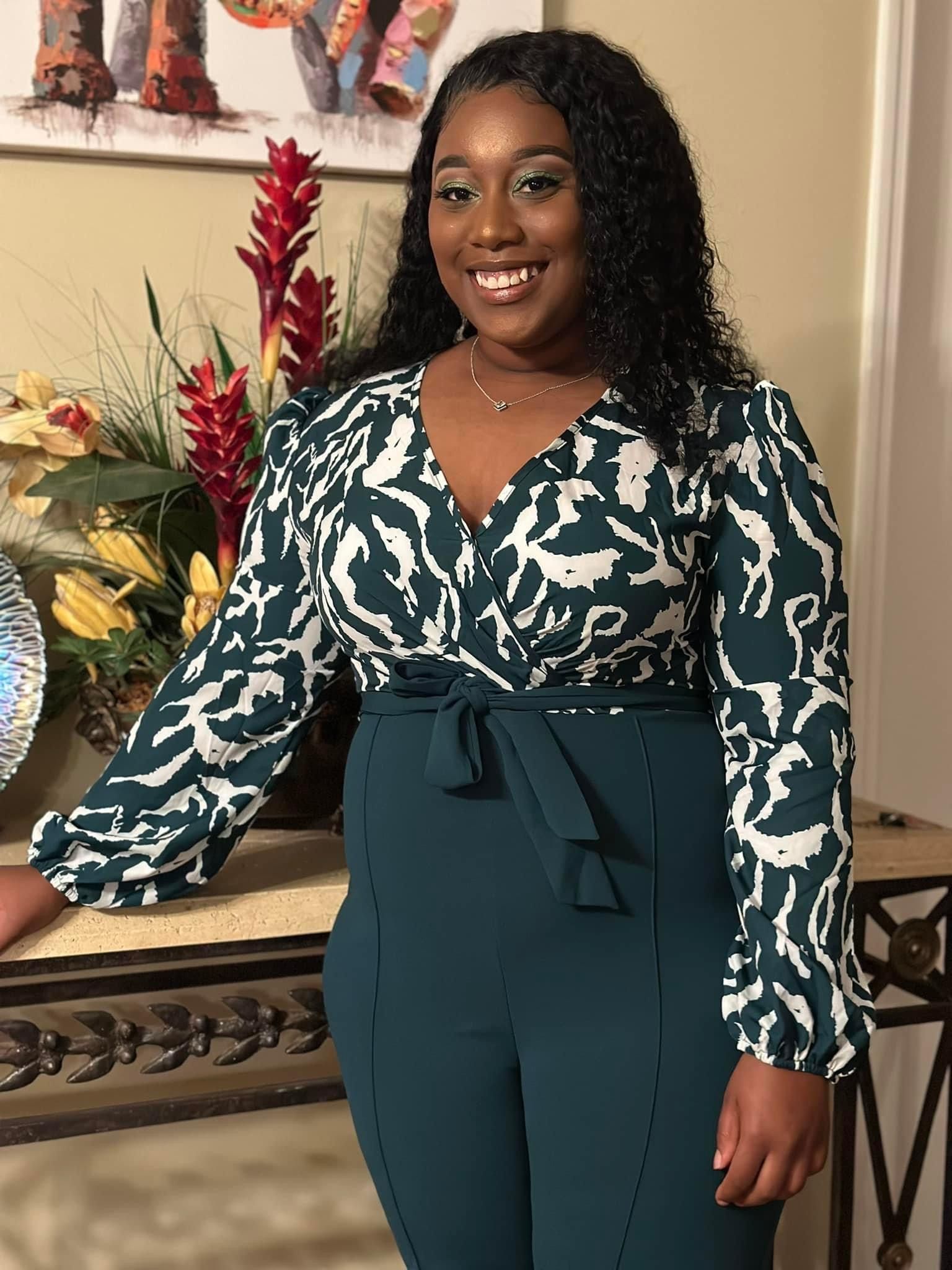 A woman in a green and white jumpsuit is standing in front of a table.