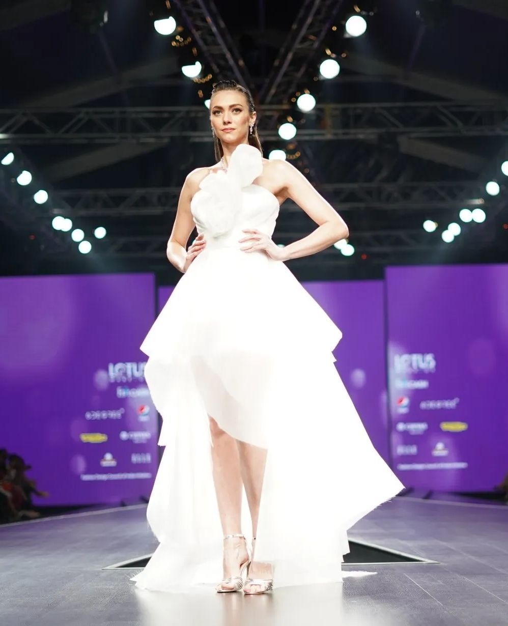 A woman in a white dress is walking down a runway