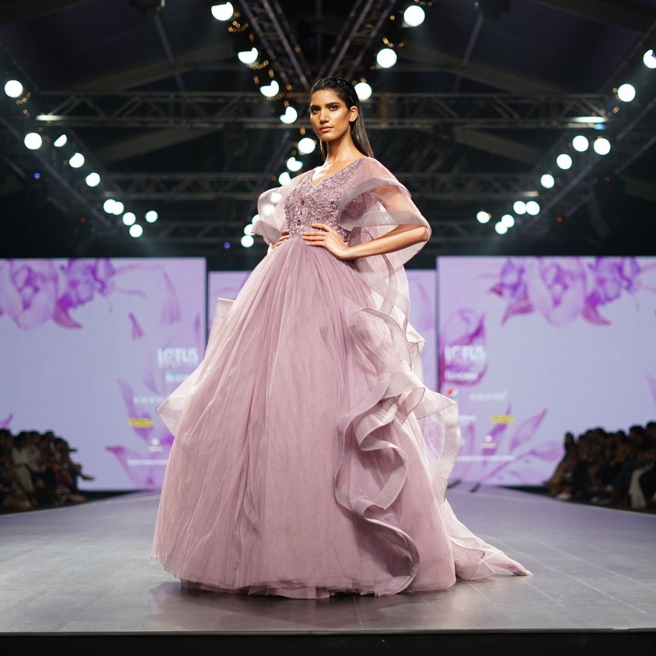 A woman in a long pink dress is walking down a runway