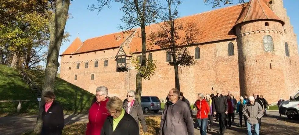 En gruppe mennesker går foran en stor murstensbygning.
