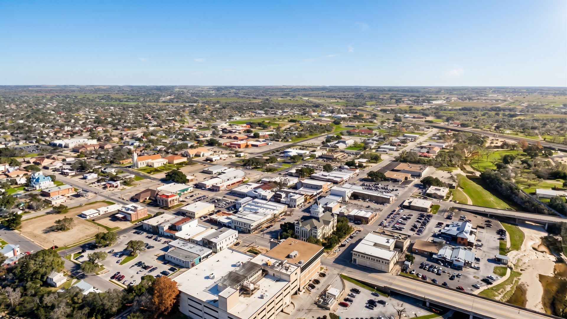 Aerial view of a suburban neighborhood with houses, streets, and a distant city skyline under a clear blue sky
