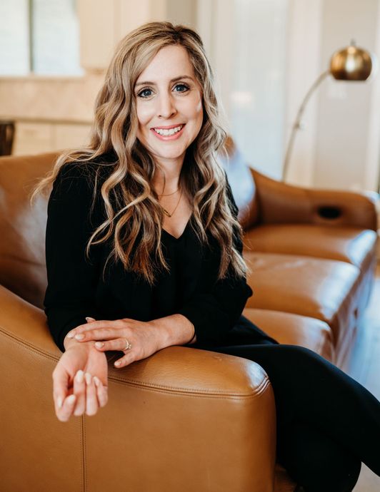 Lisa Marroquin Smiling woman in black outfit seated on tan leather sofa in a bright living room