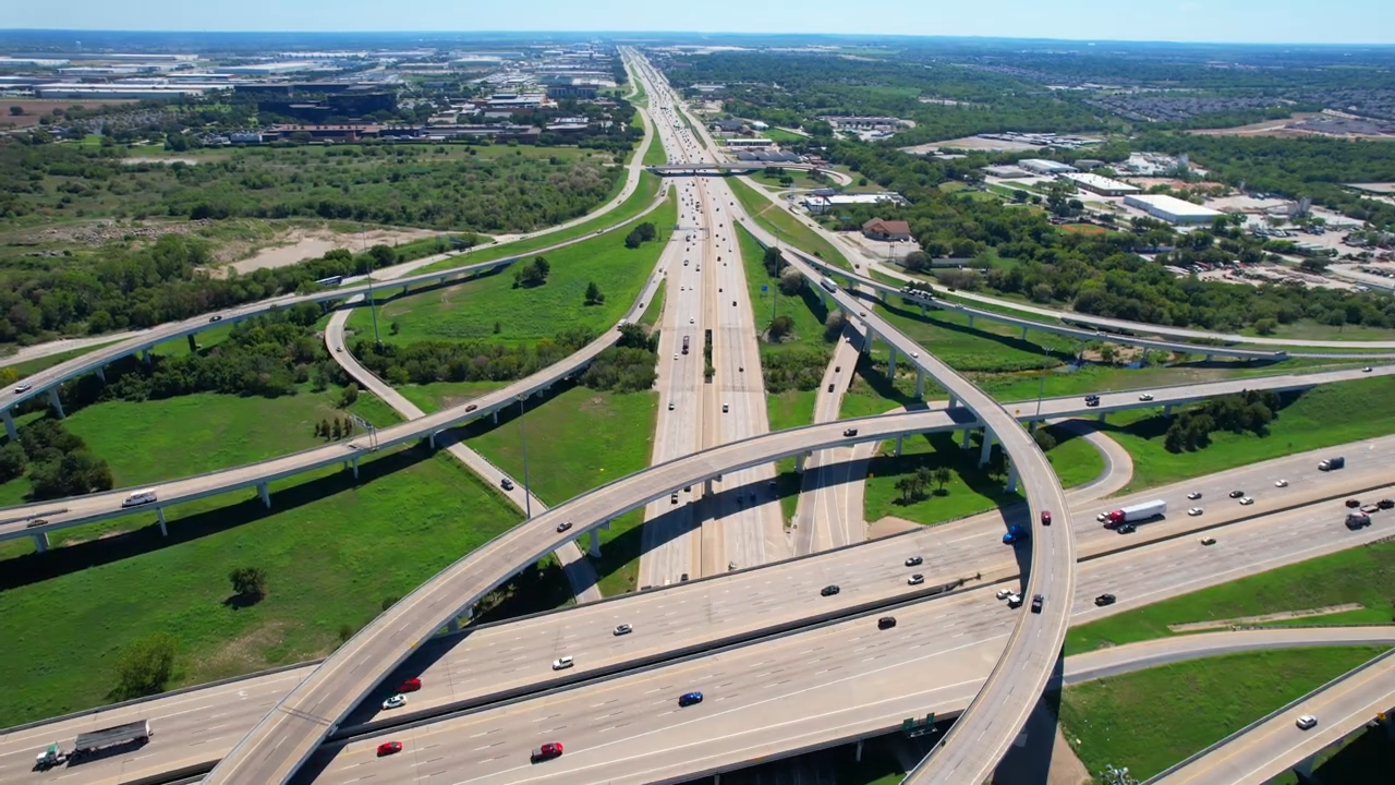 Aerial view of a highway interchange with looping ramps, green medians, and light traffic under clear skies