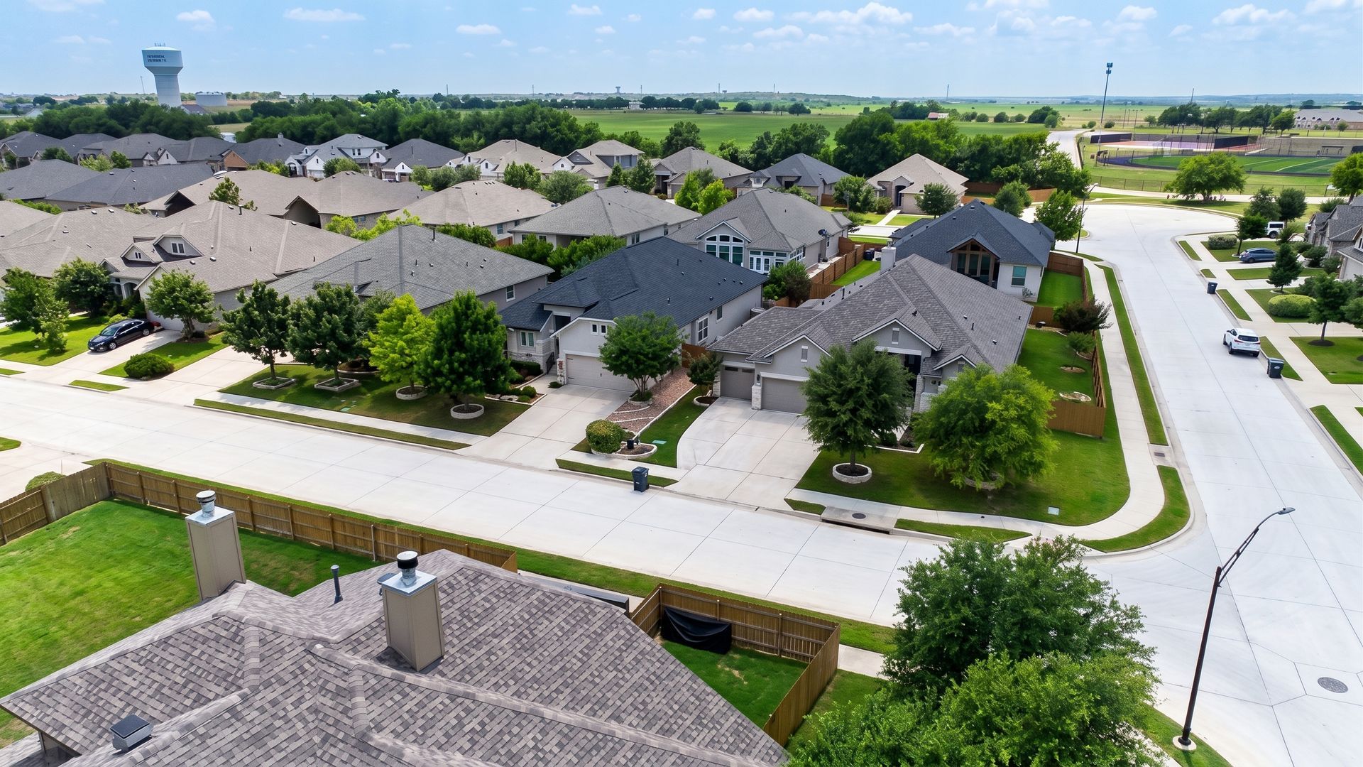 Aerial view of a suburban neighborhood with gray-roofed houses, tree-lined streets, and a water tower in the distance