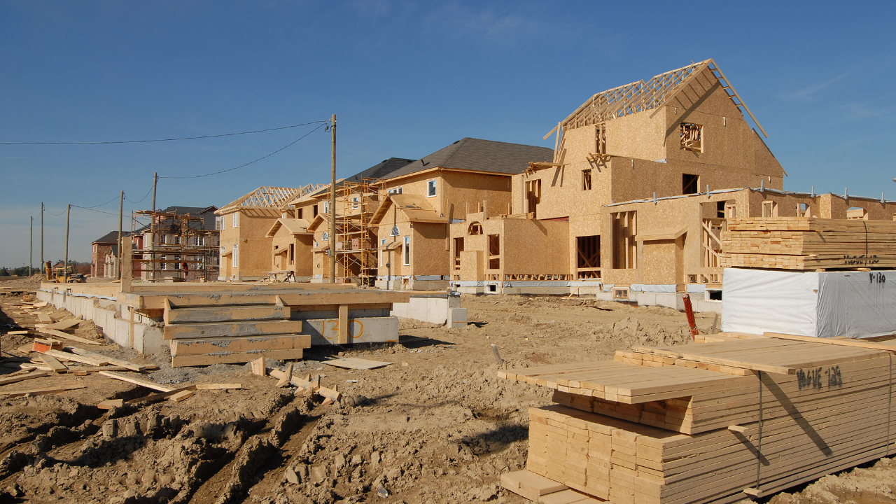 Partially built suburban homes with exposed wood framing under a clear blue sky