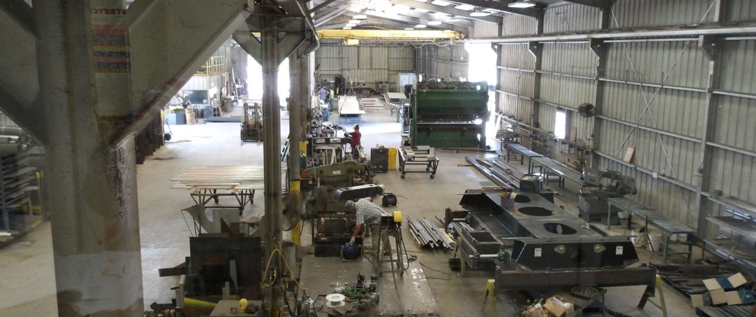 Interior of a large workshop with machinery and workers, natural light.