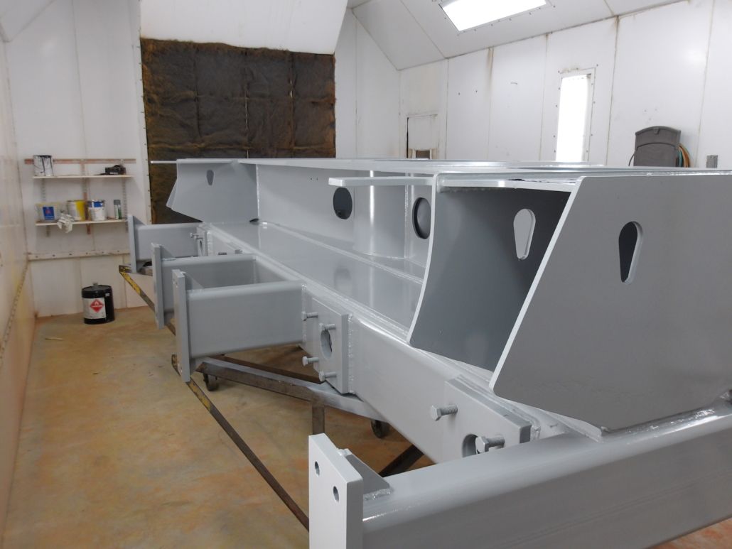 A large, gray painted metal structure inside a white paint booth.