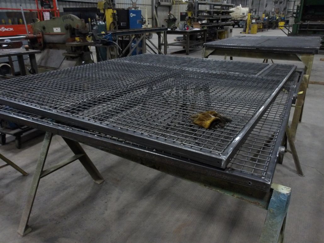 Two metal grate panels stacked on sawhorse in a workshop.