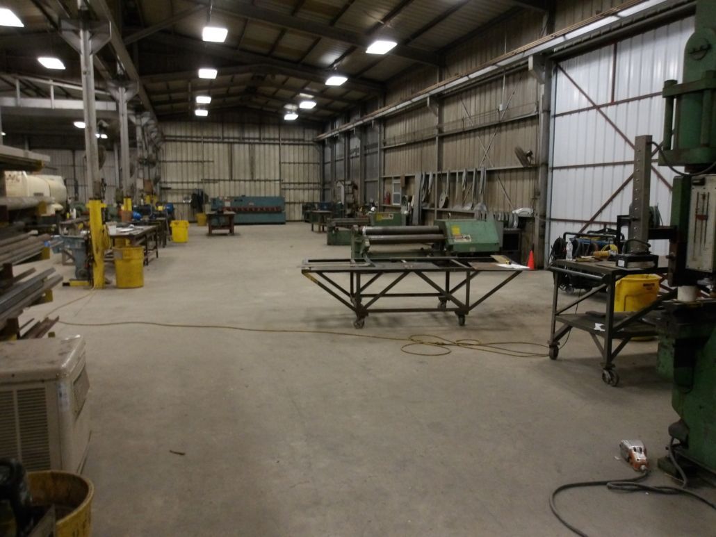 Large industrial workshop interior with various machinery and tools, concrete floor, overhead lighting.