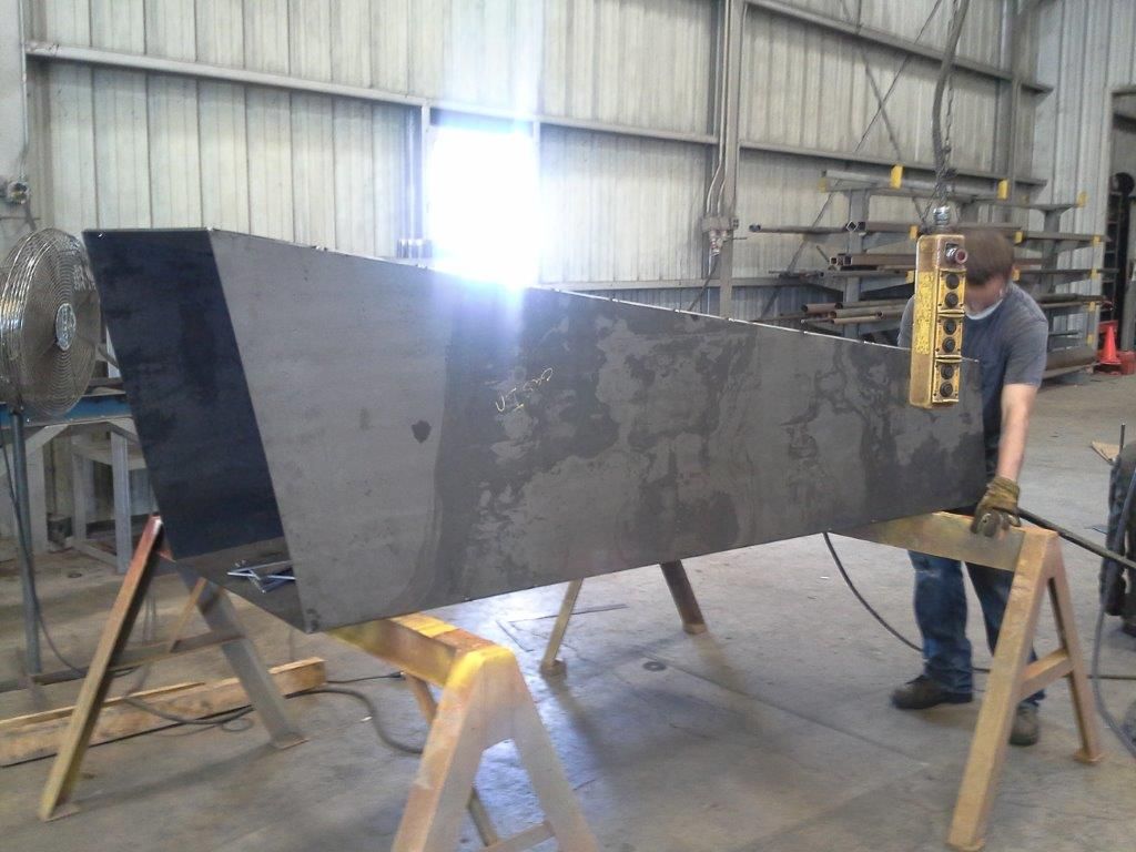 Person using a crane to move a large, angular, metal structure in a workshop.