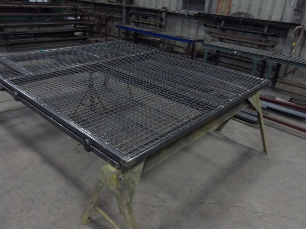 Metal grating in a rectangular frame, resting on a yellow sawhorse in a workshop.