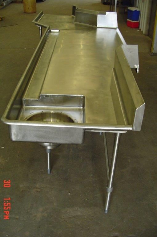 Stainless steel industrial work table with sink and built-in gutters.