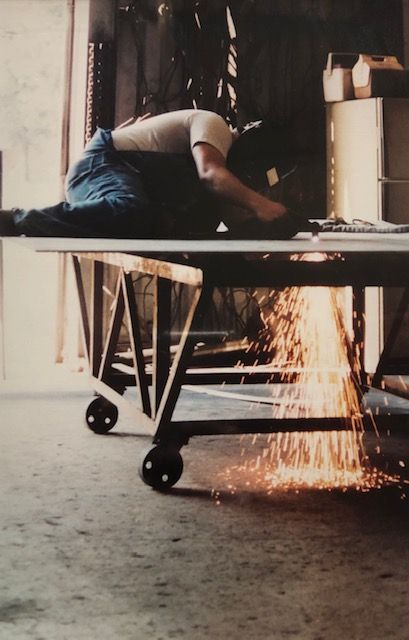 A person welding metal in a workshop, sparks flying. They wear a helmet and coveralls.