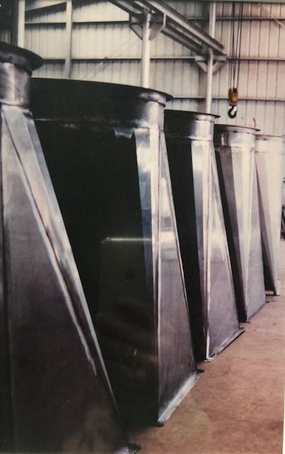 Four large, stainless steel industrial ductwork sections lined up in a warehouse.