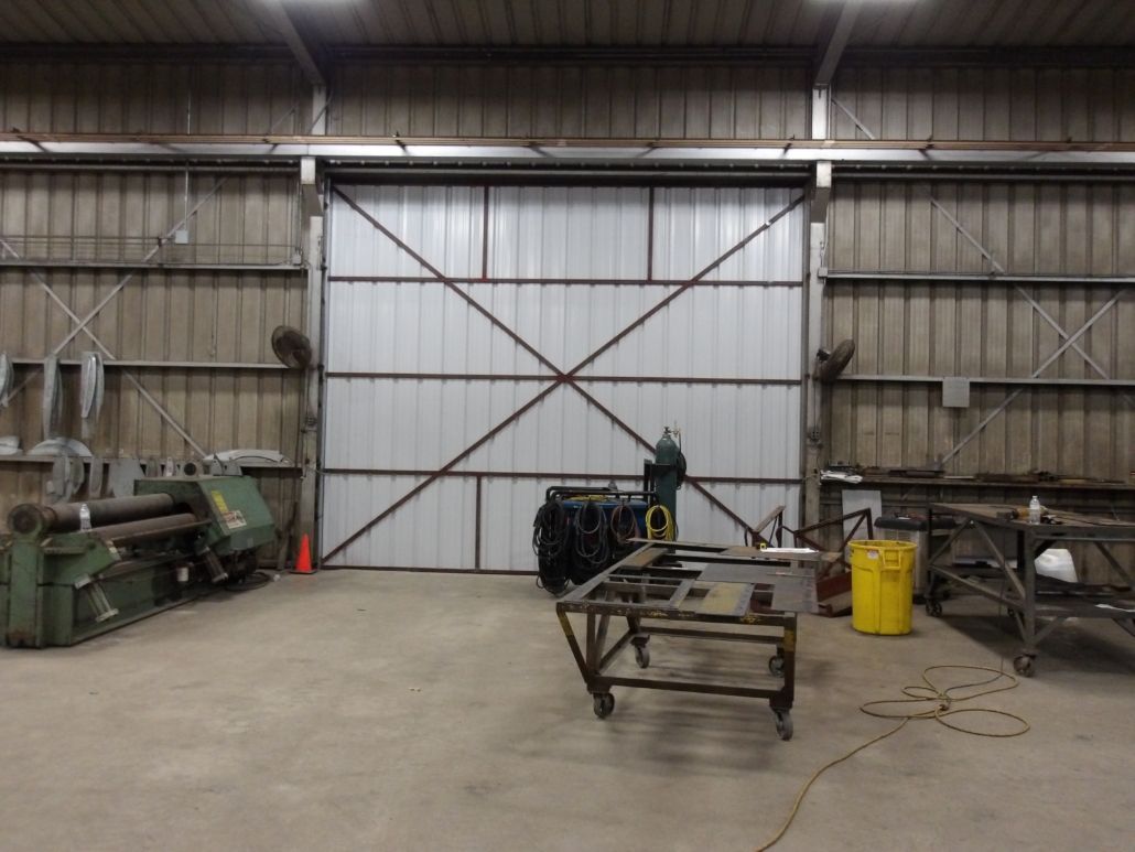 Large industrial workshop with a closed metal door, metal tables, and equipment.