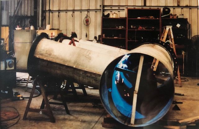 Large metal tube with blue propeller inside, resting on sawhorses in a workshop.
