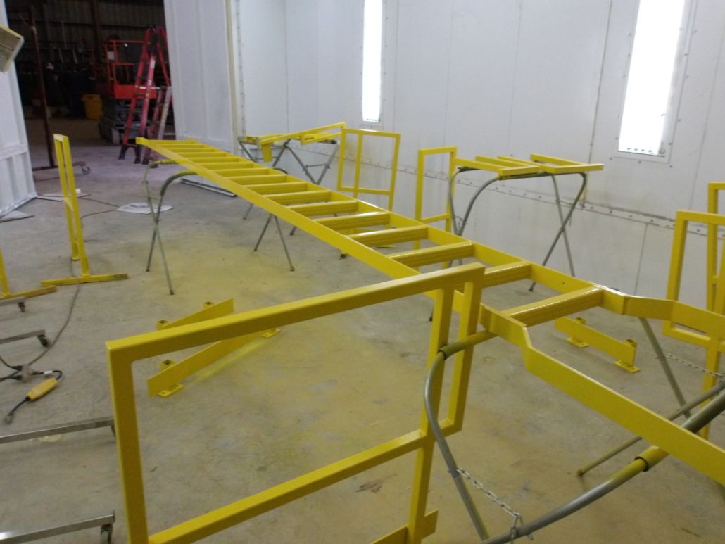 Yellow painted metal scaffolding and ladder in a paint booth.