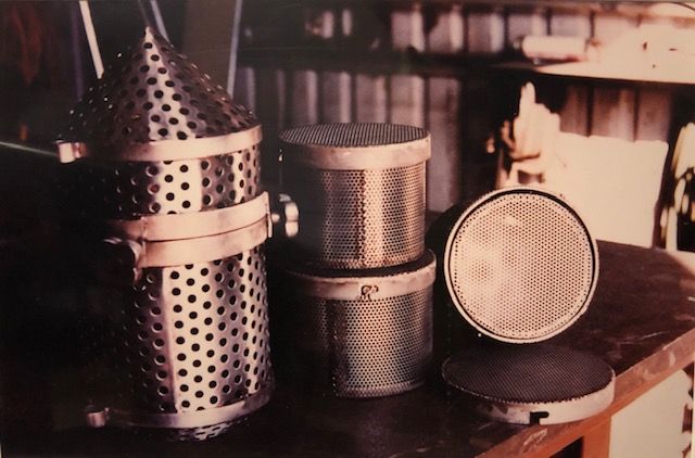 Perforated metal cylinders and cone shapes on a wooden surface; industrial parts.