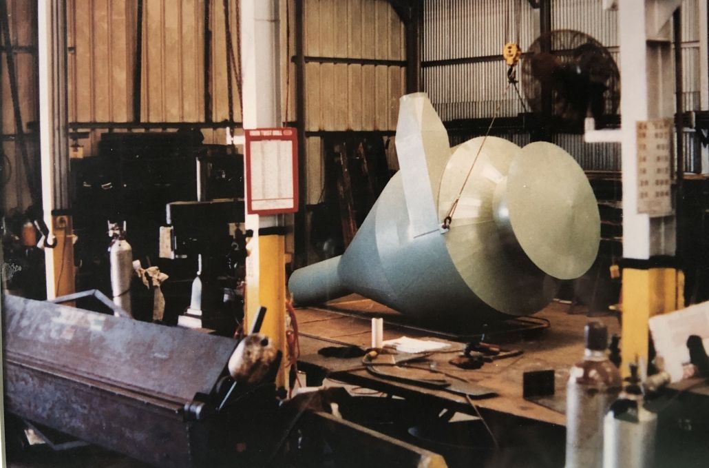 A large, light-green object, possibly a tank, suspended in a workshop.
