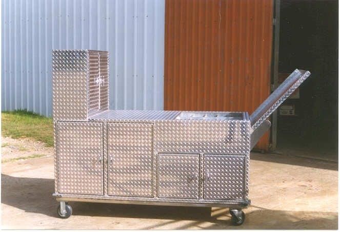 Diamond-plated metal tool chest on wheels, with multiple compartments and a top-opening lid, set outdoors.