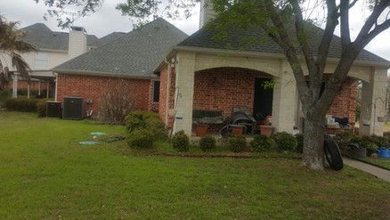 A brick house with a porch and a tree in front of it.