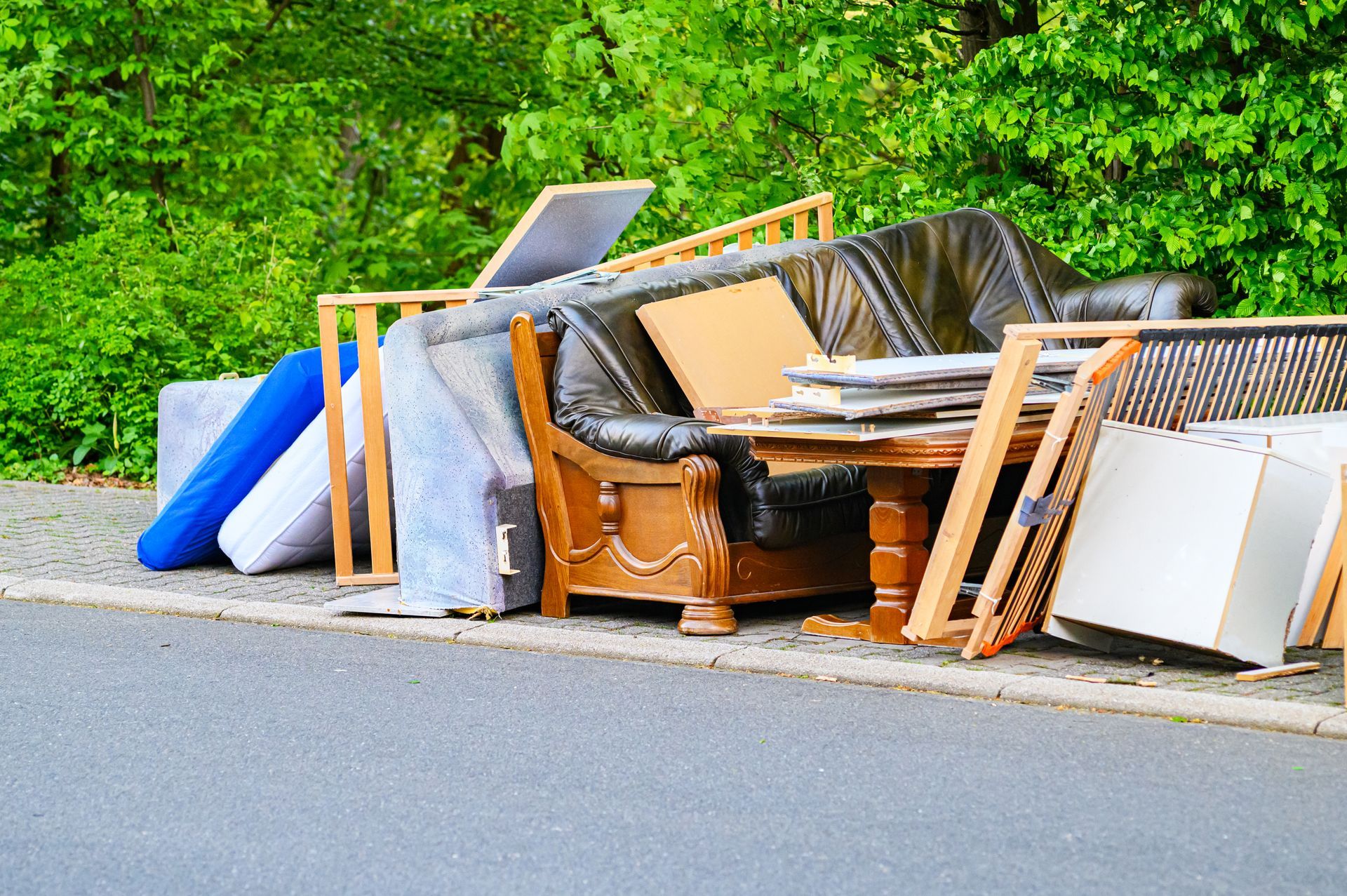 Discarded furniture and mattresses piled on a curb for bulk waste pickup.