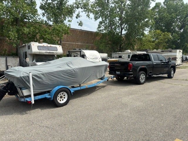 A black pickup truck parked in an outdoor lot, towing a boat covered with a gray tarp on a blue trailer.