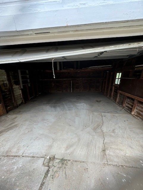The interior of a dark, unfinished garage with a concrete floor and a partially open white door.