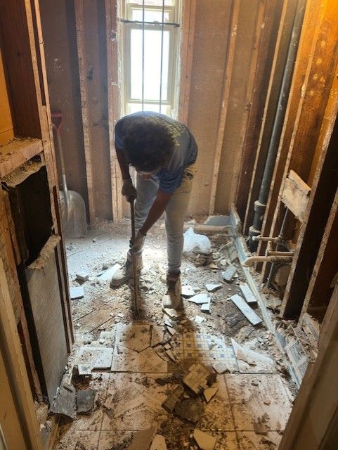 A person in work clothes uses a broom to sweep debris from the floor of a room undergoing construction or renovation.