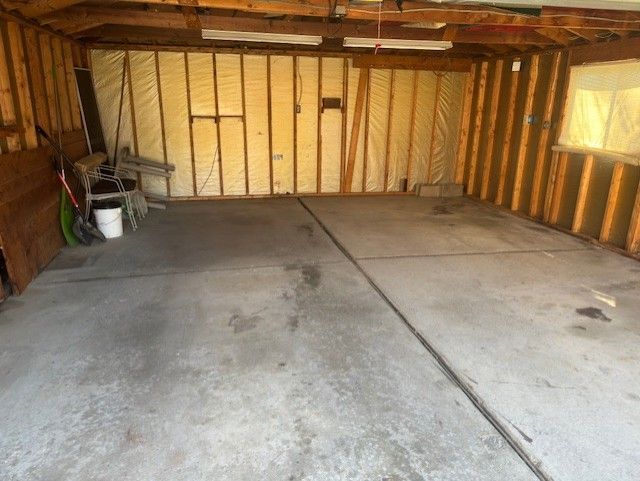 An interior view of an unfinished two-car garage with bare wooden studs, insulated walls, and a concrete floor.