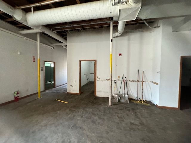 An unfinished interior space with white walls, exposed ceiling ductwork, two yellow pillars, and construction tools.