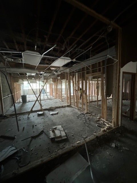 An interior view of a commercial space under construction with exposed wooden framing and suspended ceiling grid remnants.