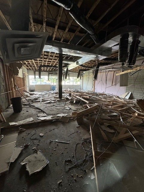 An interior room under construction with exposed ceiling joists, scattered wood debris, and visible ductwork.