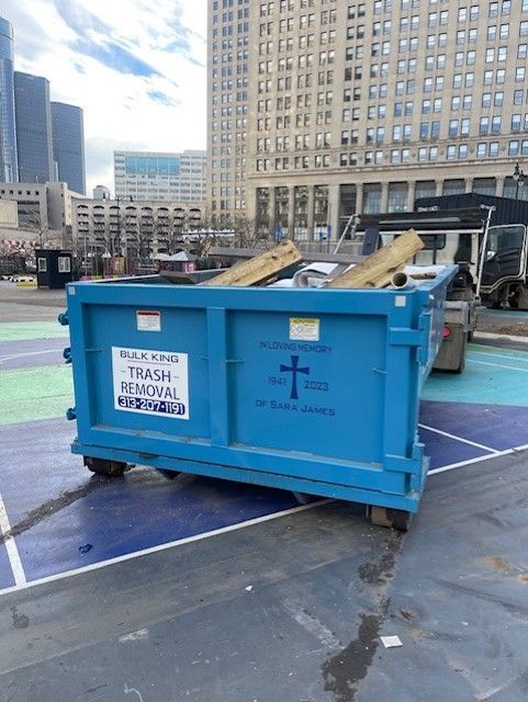 A blue trash removal dumpster sitting on a painted ground surface in front of a tall city building.