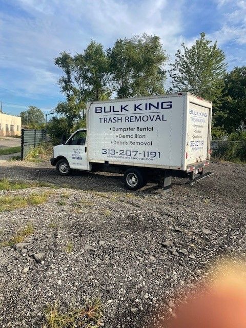 A white Bulk King Trash Removal box truck parked on a gravel lot under a partly cloudy sky.