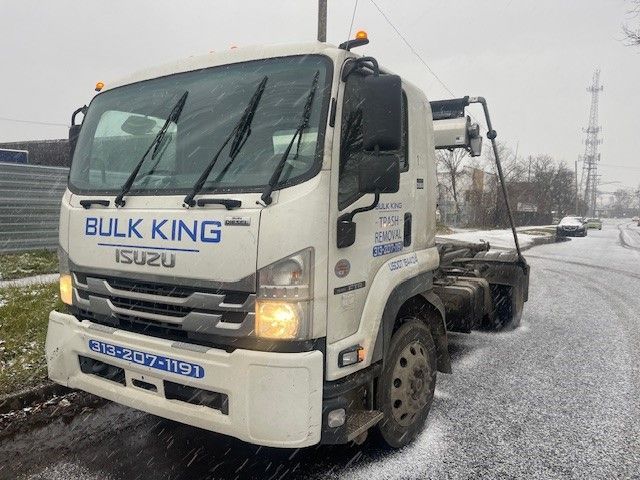 A white Bulk King Isuzu hooklift truck parked on a snowy, grey-sky roadside.